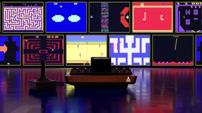 Atari 2600+ mit Joystick, dahinter mehrere Bildschirme mit Spieleszenen 